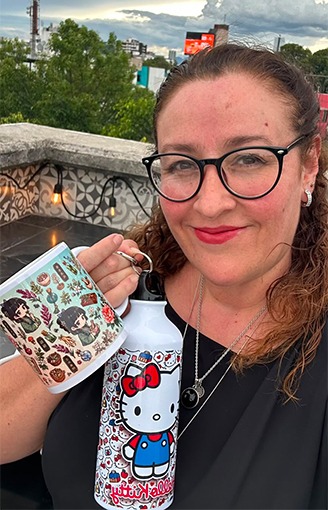 Una mujer sonriente sostiene una botella de agua de Hello Kitty y una taza de café estampada en una