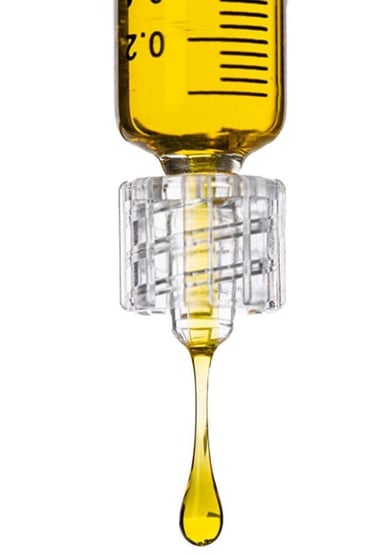 Close-up of a medical syringe dripping yellow liquid oil against a white background.