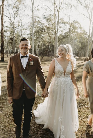 a bride and groom walking down a path in a wooded area