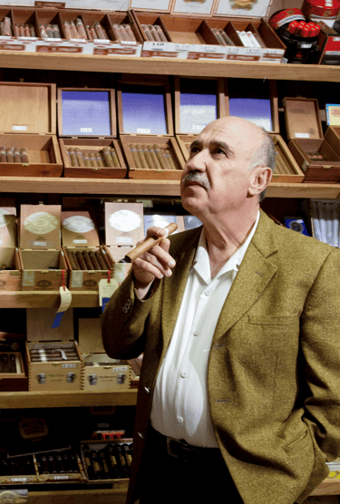 Un homme debout en costume et cravate avec à la main un cigare