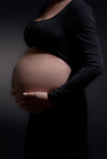 Maternity photo of a pregnant woman in a black dress holding her baby bump against a dark background.