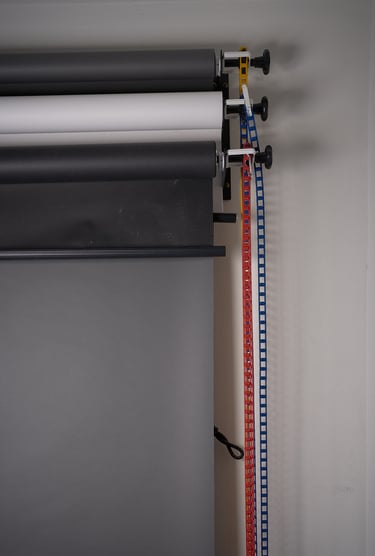 A wall-mounted studio backdrop support system with grey and white paper rolls and manual pulley chains.