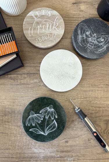 Custom engraved stone coasters with floral and butterfly designs made using a rotary diamond burr tool.