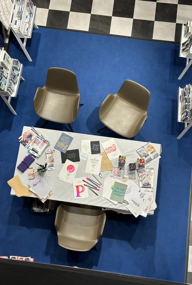 Top-down view of a stationery workshop table with modern chairs, calligraphy cards, and colorful pens.