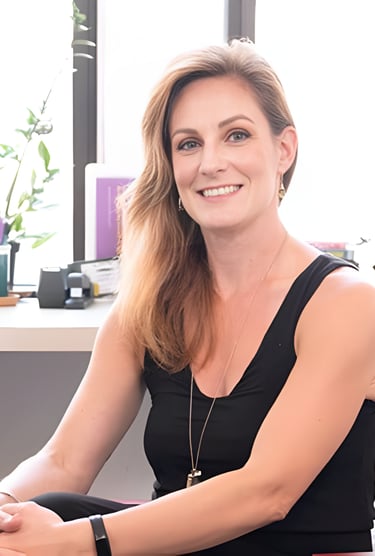 Smiling female professional in a black sleeveless top sitting in a bright modern office.