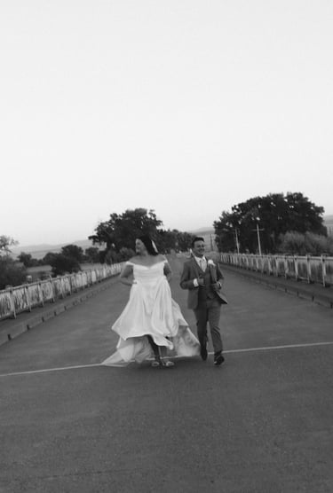 black and white photo of a bride and groom running on a bridge