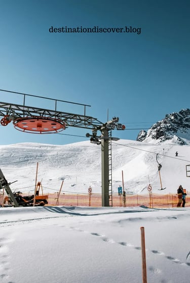 A snowy mountain scene featuring ski lift infrastructure and slopes. The foreground shows part of th