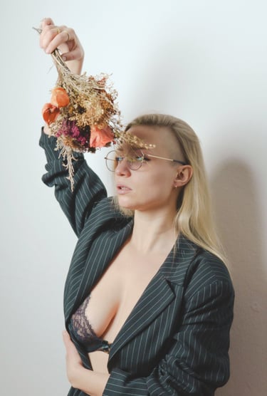 a woman in a suit and glasses holding a bouquet posing for a photo