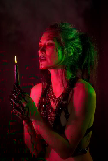 a woman wearing a harness, green and red light on her skin, holding a candle