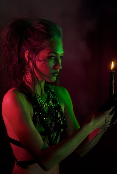 a woman wearing a harness, green and red light on her skin, holding a candle