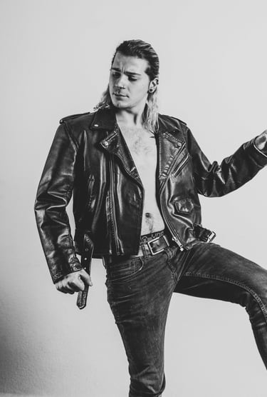 a man in a leather jacket and jeans posing for a photo