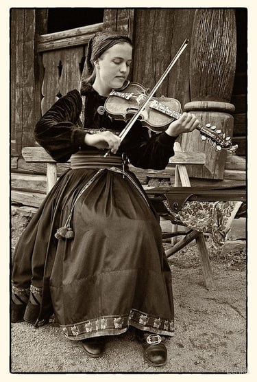 A black and white photo of a woman in traditional dress playing a hardanger violin