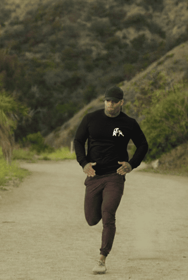 Hombre atlético trotando al aire libre, vistiendo una camiseta negra de manga larga y cachucha.