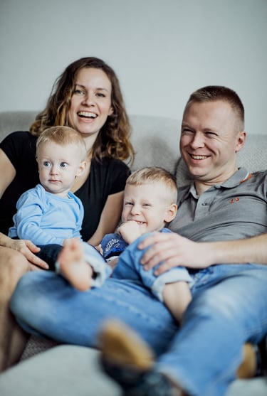 Kobieta i mężczyzna siedzą na kanapie z dwójką chłopców. Śmieją się.