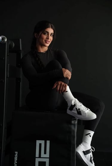 Mais Alhajri in black sportswear and white sneakers sitting in a gym setting, fitness and strength training concept."