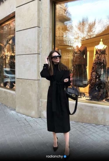 a woman in a black dress and sunglasses is standing in front of a store window