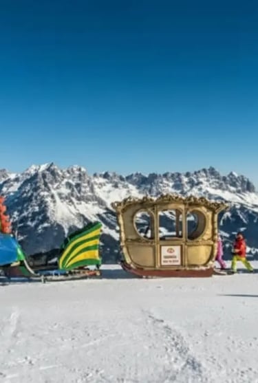 A decorative golden carriage sitting on a snowy mountain plateau with a backdrop of the jagged Wilde