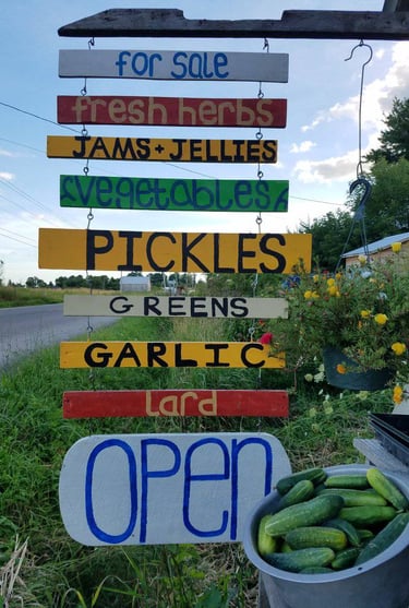 A farm stand with hand painted sign that says for sale: fresh herbs, jams and jellies, vegetables,