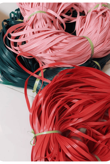 Colorful recycled plastic weaving strips in red, pink, and green prepared for handmade woven bag crafting at Craftvitas