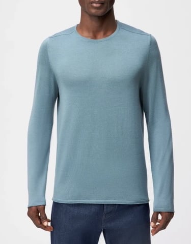 a man in a blue sweater and jeans standing in front of a white background