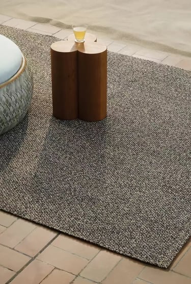 Outdoor rug adding soft texture to a balcony reading corner with natural tones and cozy outdoor styl