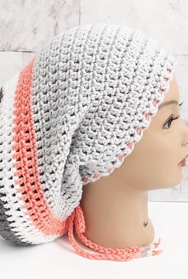 Woman wearing a large Rasta tam, locsock in light gray with orange, white, and medium gray stripes. 