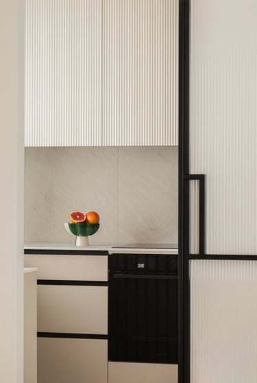 Nowoczesna kuchnia, białe ryflowane fronty szafek i misa z owocami.