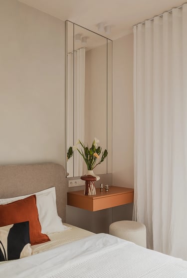 Sypialnia: wisząca szafka ruda, wysokie lustro i wazon z kwiatami.