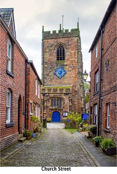 A church tower approached from a cobbled street of terraced houses