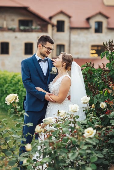 Couple de Mariés qui se regardent tendrement derrière un buisson de roses blanches.