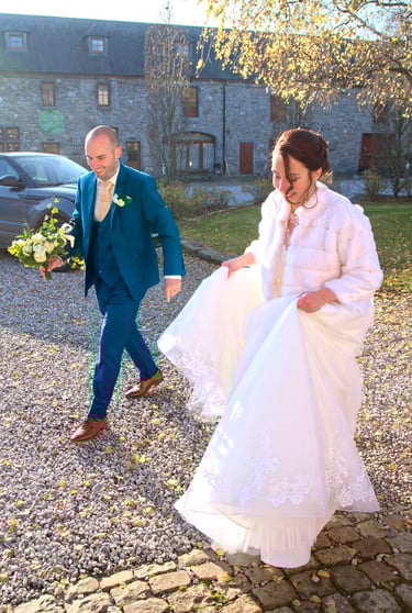  Une mariée souriante vêtue d'un manteau de fourrure blanche et un marié en costume bleu se promène.