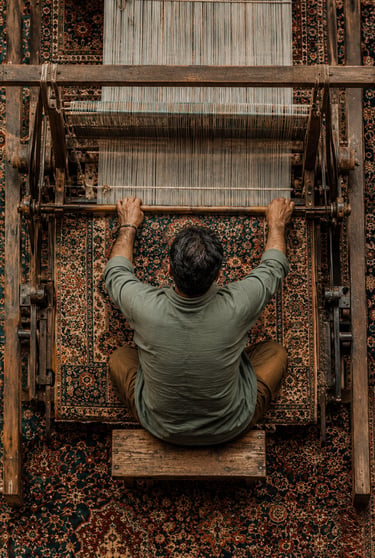 A skilled weaver operates a traditional wooden handloom to create an intricate Persian rug.