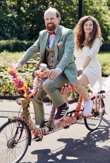 Smiling bride and groom on a tandem bicycle.