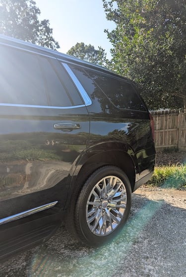 Rear profile of a black GMC Yukon SUV featuring chrome wheels and polished trim in sunlight.