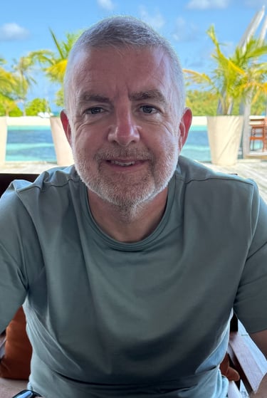 "Person seated at outdoor table in tropical resort with palm trees and lounge chairs nearby