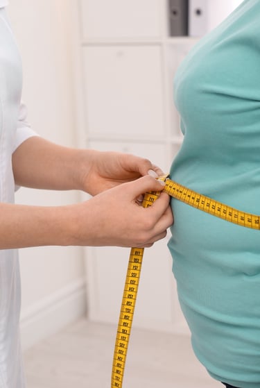 A doctor measuring a patient's waist with a yellow tape measure during a weight loss consultation.