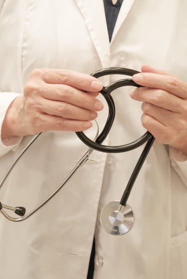 Close-up of a healthcare professional in a white lab coat holding a black medical stethoscope.