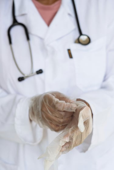 A healthcare professional in a white lab coat putting on sterile medical gloves for a procedure.