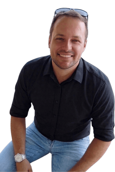 A smiling man wearing a black button-down shirt, blue jeans, and sunglasses on his head.