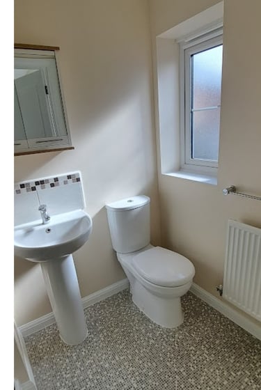 Modern small bathroom with a white pedestal sink, toilet, mosaic floor tiles, and a privacy window.