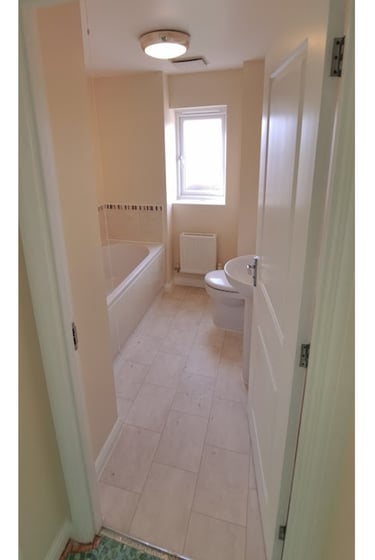 Modern small bathroom with a white bathtub, toilet, sink, and tiled floor seen through a doorway.