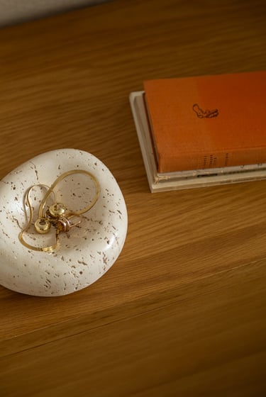 Kamienna misa z trawertynu ze złotą biżuterią na drewnianej szafce.