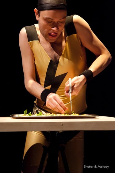 Ein Schauspieler in einem gelben Overall mit einer Salatschneidemaschine auf der Bühne.