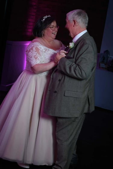 Smiling bride and groom enjoying their first dance at a wedding reception with purple lighting.