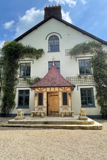 Traditional English manor house with a timber-framed porch, stone lion statues, and climbing ivy.