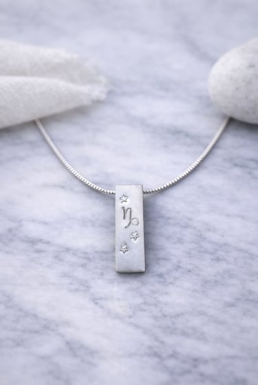 Handmade 999 silver Capricorn zodiac necklace with a vertical bar pendant on a marble surface.