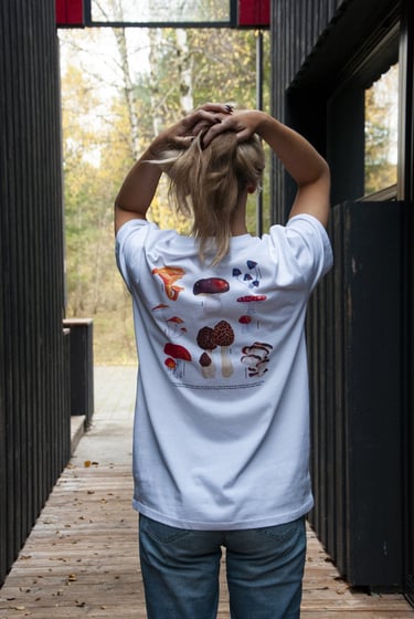 a woman in a white shirt and handdrawn mushroom illustration and jeans standing on a wooden deck