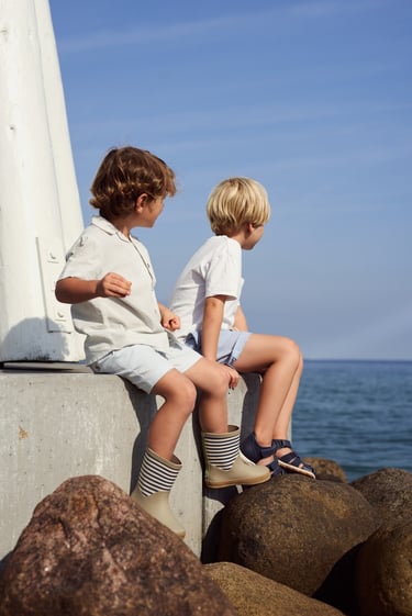 Wheat SS25 campaign imagery featuring 2 young boys sitting by the sea, wearing Wheat clothing and footwear
