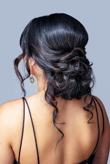 Woman with textured low bun updo and loose curls wearing black strappy dress, elegant hairstyle perfect for wedding or prom.