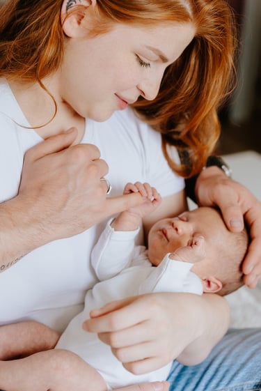 plan rapproché d'un bébé dans les bras de sa mère qui tiens un doigt de son père